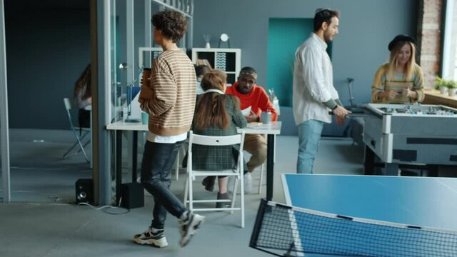 Young businesswoman is walking in open space office while colleagues are playing foosball and working together. Business center and activities concept.