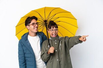 Young mixed race couple holding an umbrella isolated on white background presenting an idea while looking smiling towards