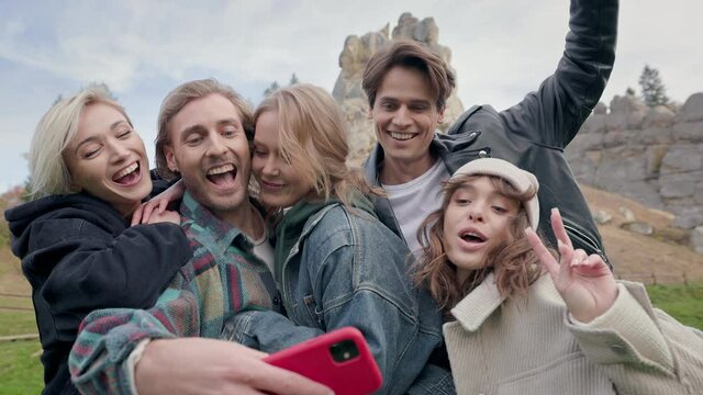 Five Friends In Nature Taking Selfie. Two Young Men And Three Women Smiling Together At Camera. Man With Beard Pulls Phone Out Of His Pocket And Others Run Him.