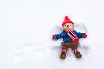 Small Outdoor Fun at Wintertime / Cute teddy bear snow angel with nostalgic knitted clothes happy in winter (copy space)