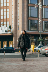 Street stylish portrait of stylish woman in oversize clothes on cityscape background, looking aside, vertical