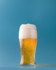 Beer with foam in a transparent glass on a blue background