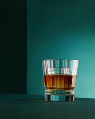Whiskey with ice in a transparent glass on a green background