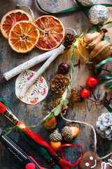 Making home made garlad from natural materials - dry orange chips, ginger bread cookies, arcons, ribbons, cinnamon sticks and pine cones, eco friendly, on wooden table with lights, flat lay