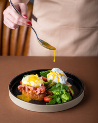 Bruschetta with bacon, poached egg and salad. Hollandaise sauce is pouring from a spoon