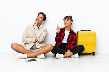 Obraz premium Young mixed race travelers couple sitting on the floor isolated on white background pointing a great idea and looking up