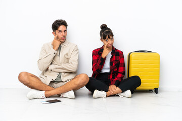 Young mixed race travelers couple sitting on the floor isolated on white background looking to the front