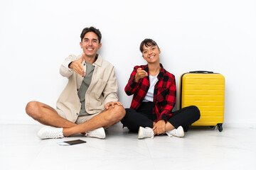 Obraz premium Young mixed race travelers couple sitting on the floor isolated on white background shaking hands for closing a good deal