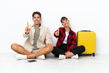 Obraz premium Young mixed race travelers couple sitting on the floor isolated on white background showing and lifting a finger