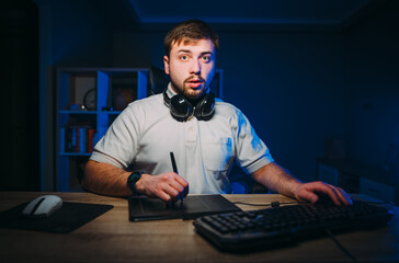 Portrait of a freelance designer working at night on a computer on a tablet with a serious face....