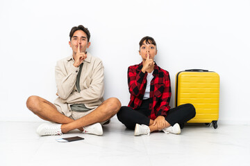 Fototapeta premium Young mixed race travelers couple sitting on the floor isolated on white background showing a sign of closing mouth and silence gesture