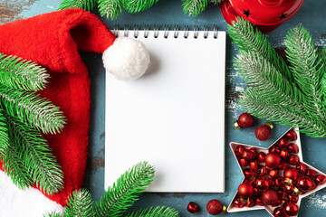 Christmas or New Year's blue festive background with an open blank notebook, fir branches and red decorations. A checklist or a letter to Santa. Top view with copy space