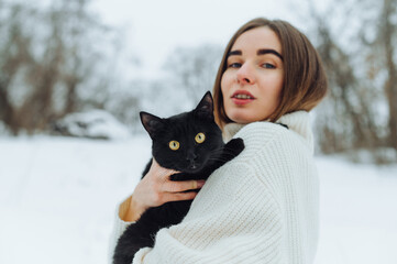 Positive lady in a white knitted sweater posing with a black cat in her arms on a white background.