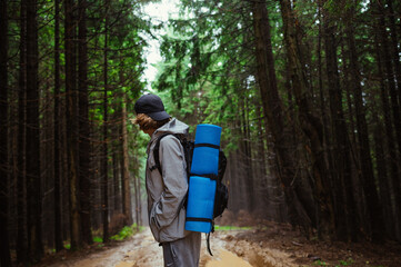 Male tourist with a backpack stands in a mountain forest after the rain and looks away. Hiker on a mountain hike.