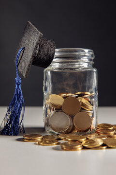 Graduation hat on jar with coins. Scholarship money concept. Vertical image