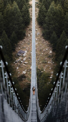 Backpacker man with yellow jacket crosses a suspension bridge in the middle of the Swiss Alps