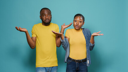 Uncertain people raising shoulders and not knowing to answer question in studio. Man and woman in...