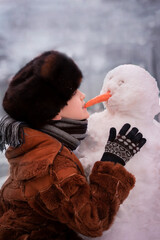 child playing with snow. Little boy biting nose of a carrot in a snowman. The child is making a snowman. Winter fun.