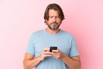 Senior dutch man isolated on pink background using mobile phone