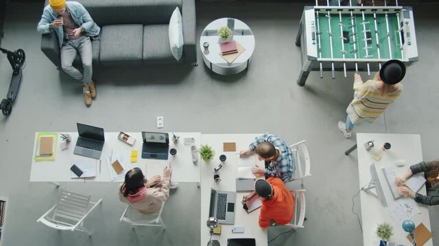 Top view of employees youth working and playing foosball game in modern open space office. Comfortable workplace and business concept.