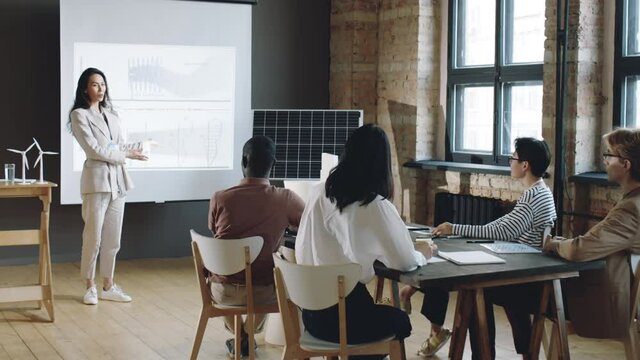 Businesswoman standing by whiteboard and giving presentation about renewable energy to group of multiethnic colleagues during seminar