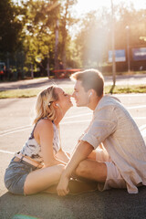 Naklejka premium summer holidays, technology and people concept - happy couple with earphones listening to music and touching noses on basketball playground