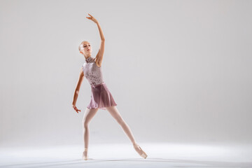 Fototapeta na wymiar Beautiful young girl ballerina in pointe shoes and pink swimsuit on light background.