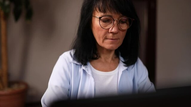 Mature woman writer or jiurnalist in glasses typing on laptop article