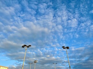 Lights posts at tennis courts agains blue sky and clouds