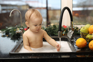 Cute blonde baby bathing in the sink in the kitchen. The baby is sitting in a foam with oranges