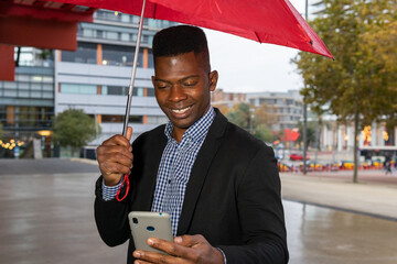 African american man with a red umbrella using the mobile. Rain concept