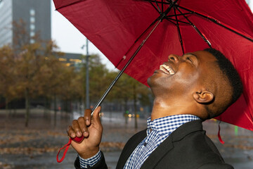 African american man protecting himself from the rain with a red umbrella. Rain concept