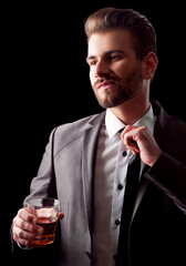 Young handsome well dressed man untiing his tie holding a glass of whiskey in his hand. Isolated on black background.