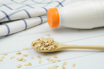 Oatmeal in in a wooden spoon and plastic bottle of oat milk. Alternative milk, healthy eating