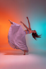 Portrait of young flexible contemp dancer dancing isolated on gradient blue orange background in...
