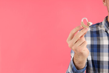 Young man hold hearing aid on pink background