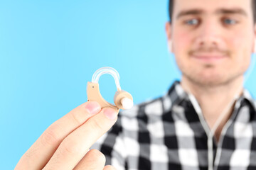 Young man holding a hearing aid on a blue background