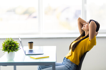 Business woman relaxing with hands behind her head and sitting on an office chair.