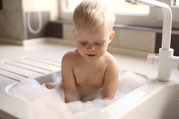 Cute blonde baby bathing in the sink in the kitchen