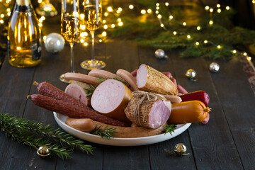 Fresh sausages and hams on new year or Christmas celebration table with champagne glasses and bokeh lights, delicious snack, spicy and high quality meat products made of pork and veal, beef.