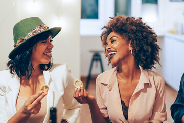 Two multiethnic young women smiling and talking together at a dining table during a dinner party...