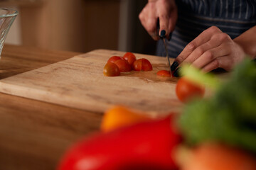 Multi-cultural young female chopping up tomatoes on wooden chopping board in kitchen. Fresh and healthy