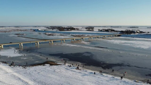 Ice skating people on a frozen Reevediep lake during a beautiful winter day in Overijssel, The Netherlands. Aerial drone point of view.