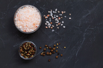 salt and pepper on a black background.Pink Himalayan salt and mix of peppers in a glasses bowls on the black background. Top view copy space. Set of various spices.