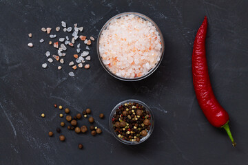 red hot chili pepper, Pink Himalayan salt and mix of peppers in a glasses bowls on the black background. Top view copy space. Set of various spices.