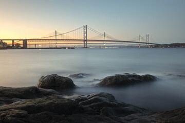View of a stone coast of the sea and bridges in the background. Forth Road Bridge and New Queensferry Crossing Bridge, Scotland, United Kingdom