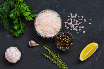 Set of various spices for cooking. fresh garlic, yellow lemon, greens, Pink Himalayan salt and mix of peppers in a glasses bowls on the black background. Top view copy space.