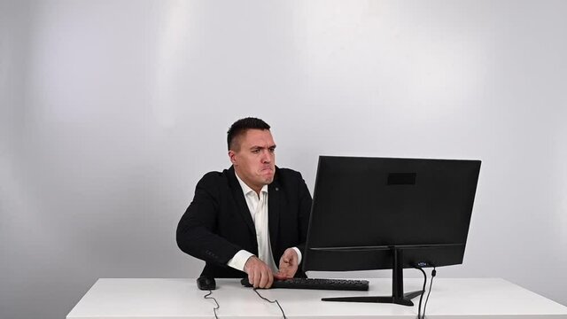 Caucasian man in a suit gets angry and smashes the keyboard on the monitor. An office worker in a rage breaks the computer.