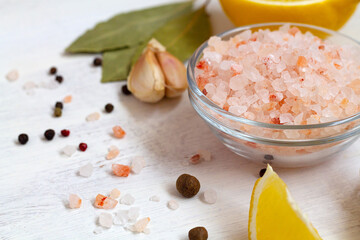 Fototapeta na wymiar salt and lemon.close-up Pink Himalayan salt on the glass bowl, piece of yellow lemon and fresh garlic on the white background with copy space. Set of various spices for cooking.