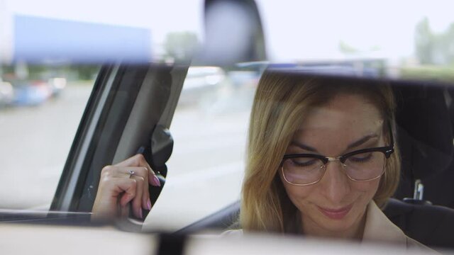 Smiling successful blond woman in stylish eyeglasses fastening seatbelt sitting on driver seat in car, going for business in her new automobile, vehicle rent or purchase, femininity